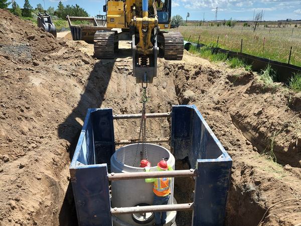 Excavator setting a manhole inside a trench box